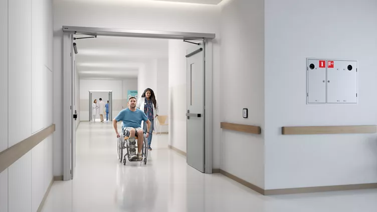 Woman pushing man in wheelchair hospital hallway